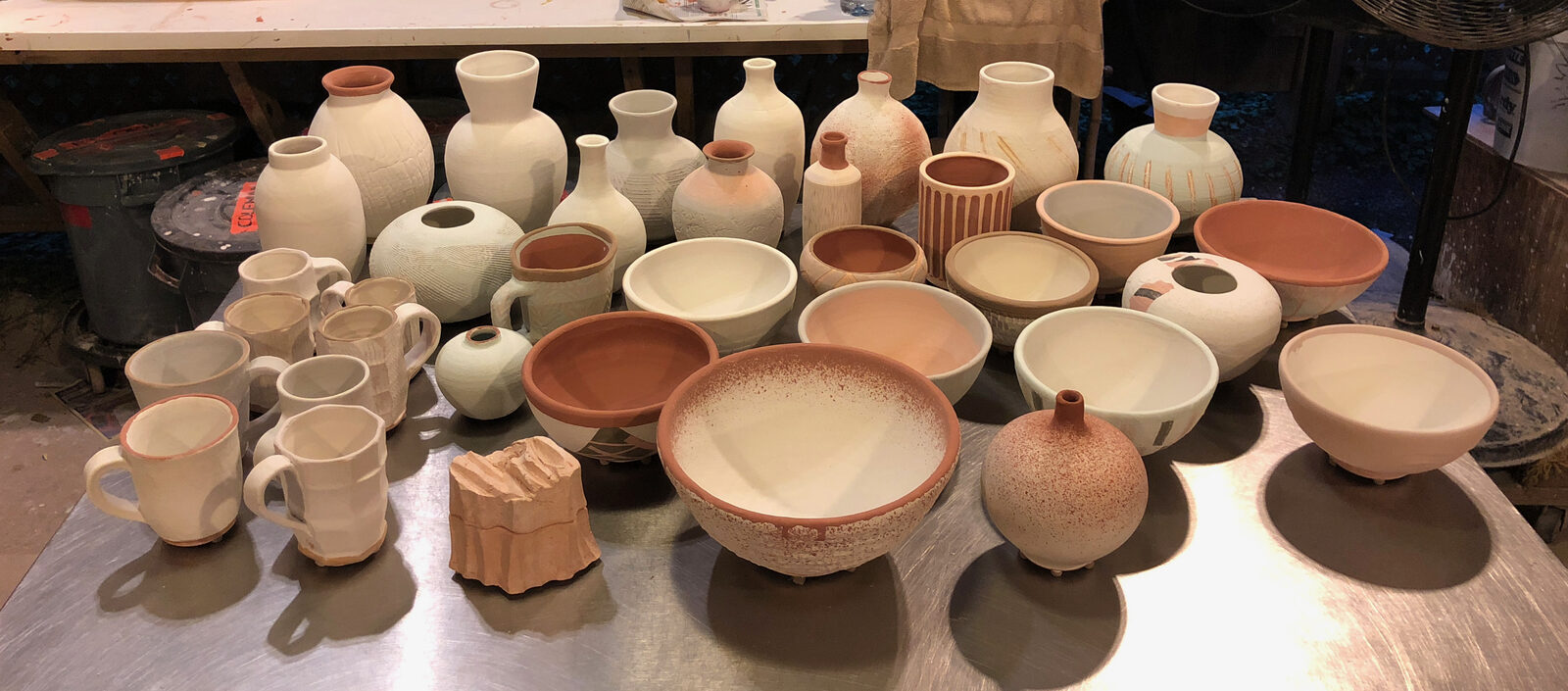 A table of unfired greenware pots in the studio