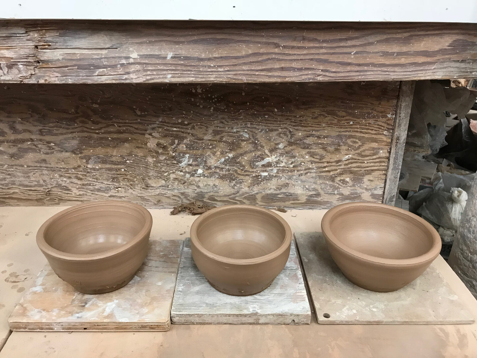 Three plain thrown bowls drying on wooden bats — the first pieces